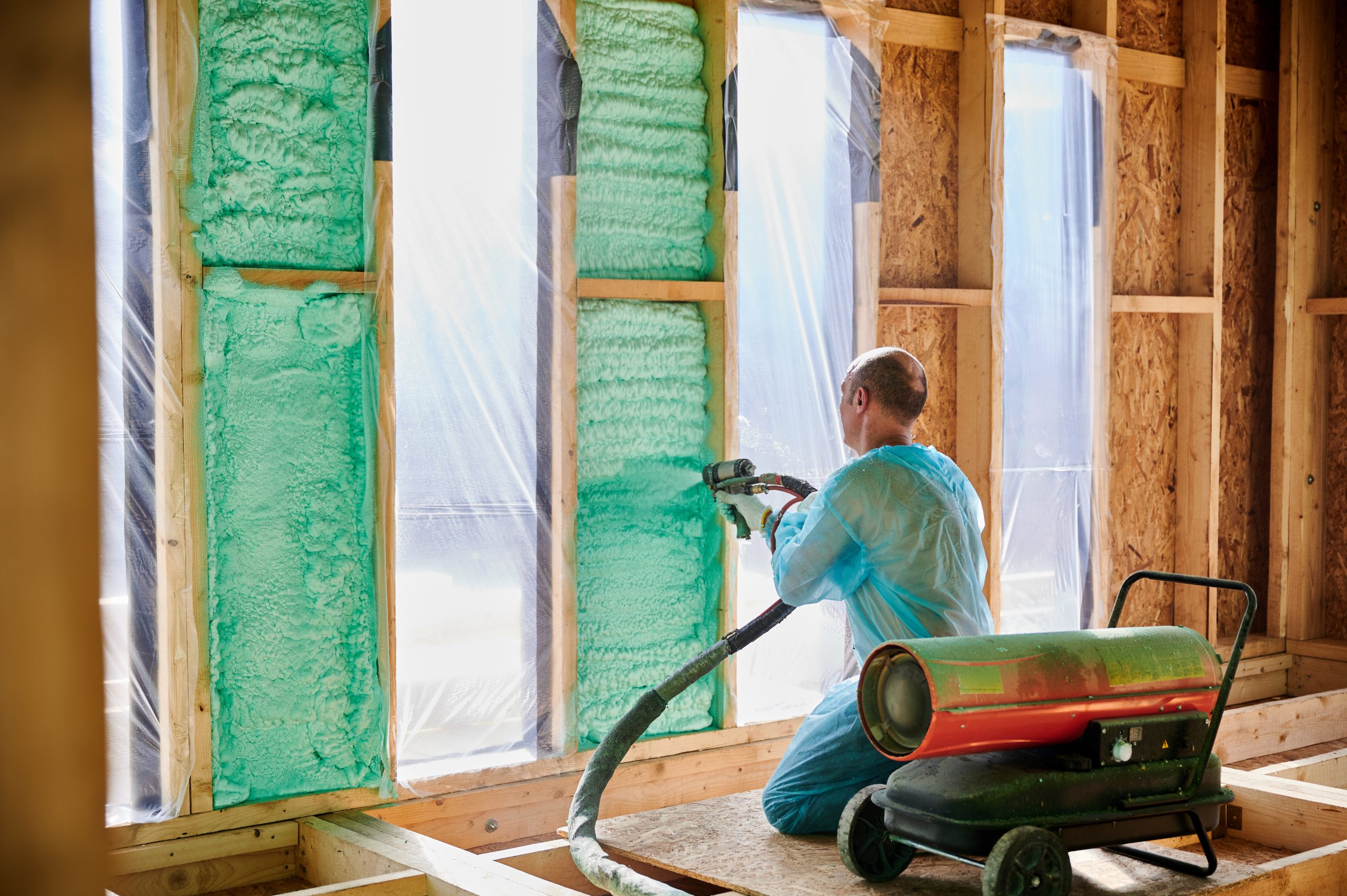 Worker spraying polyurethane foam for insulating wooden frame house. Male builder insulating wooden frame house. Man worker spraying polyurethane foam inside of future cottage, using plural component gun. Construction and insulation concept.