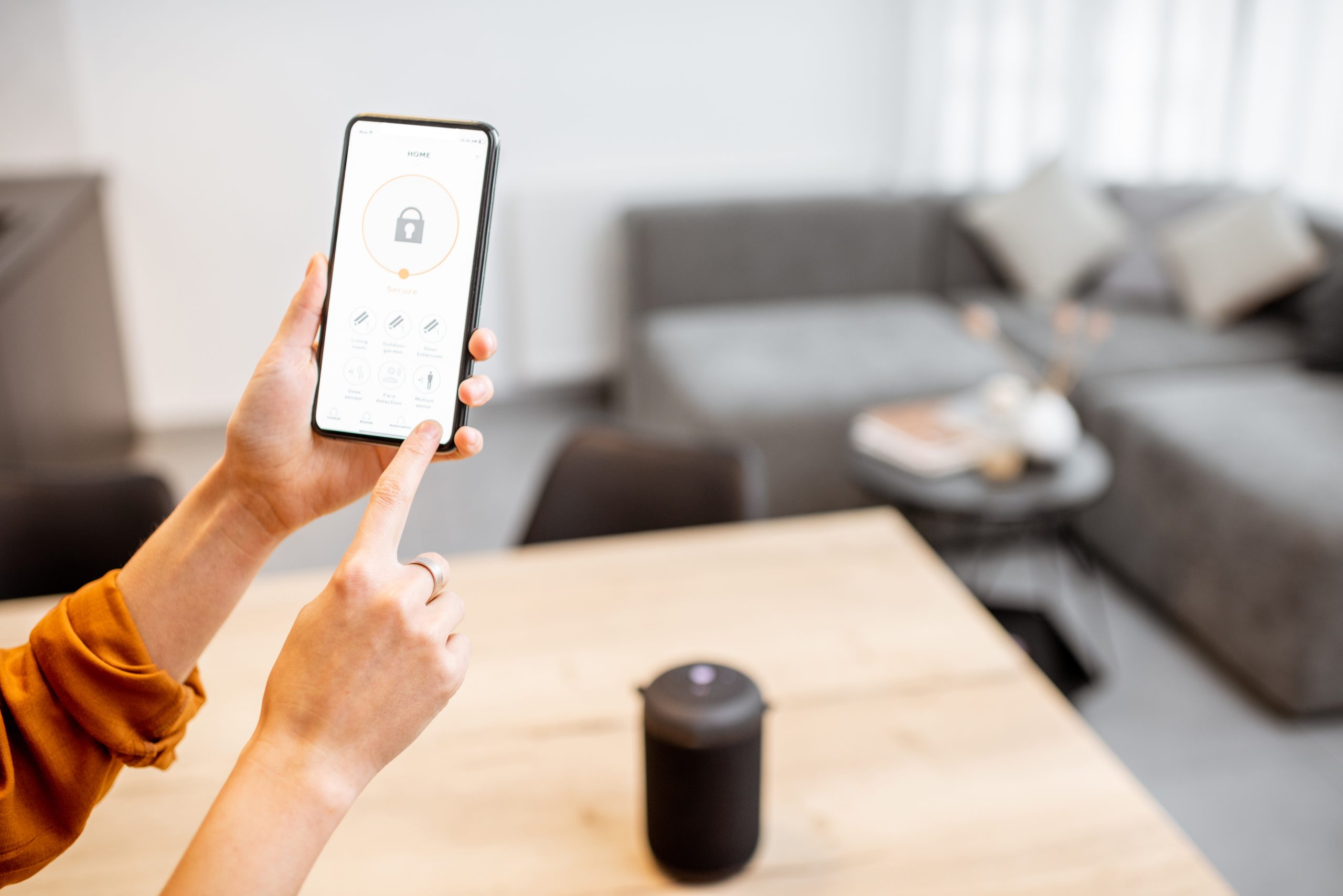 Holding a smartphone with launched security program indoors. Concept of controlling and managing home security from a mobile device